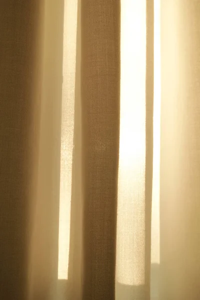Closed linen curtains hanging on window on a sunny day inside a modern home. Shadow and sunlight shining through cream cotton or beige fabric for interior decoration and copy space background.