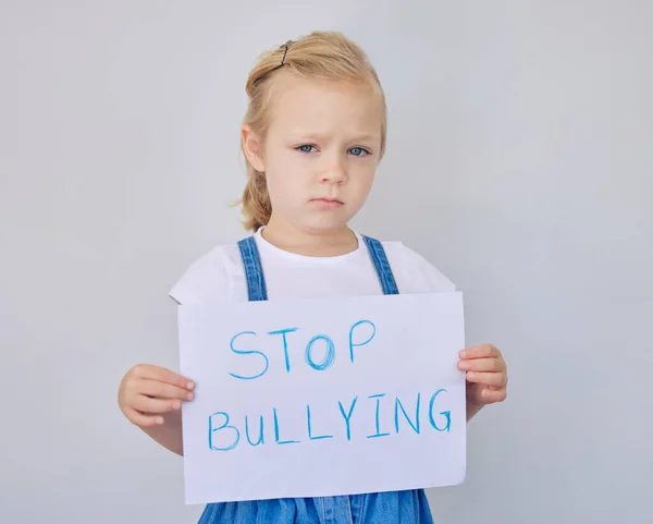 Portrait of sad little girl holding up stop bullying sign. Adorable little elementary aged girl looking sad while protesting against bullying.