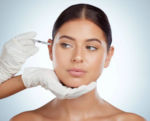 Beautiful woman getting facial fillers or botox. Young caucasian model isolated against a grey studio background with copyspace. Dermatologist injecting patient during anti ageing cosmetic procedure.