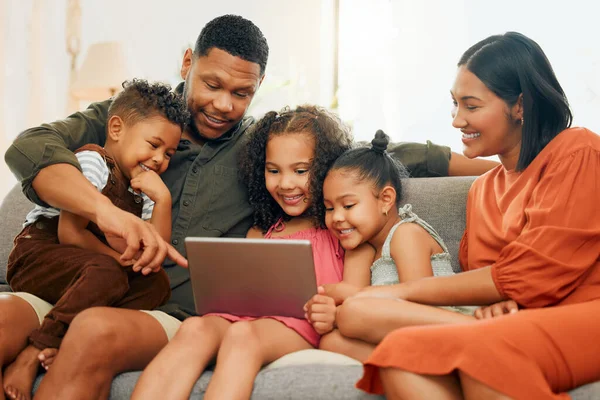 A happy mixed race family of five relaxing on the sofa at home. Loving black family being affectionate on the sofa while using a digital tablet and streaming. Young couple bonding with their kids and
