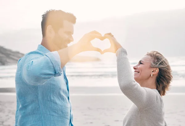 Can you feel the love. a mature couple making a heart shape with their hands at the beach