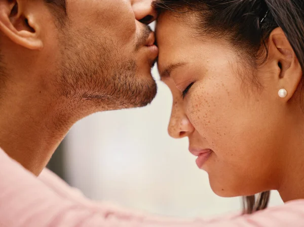 Closeup of mixed race man kissing his girlfriends forehead. Headshot of hispanic couple bonding and sharing an intimate moment at home. Beautiful woman with freckles feeling in love with boyfriend.