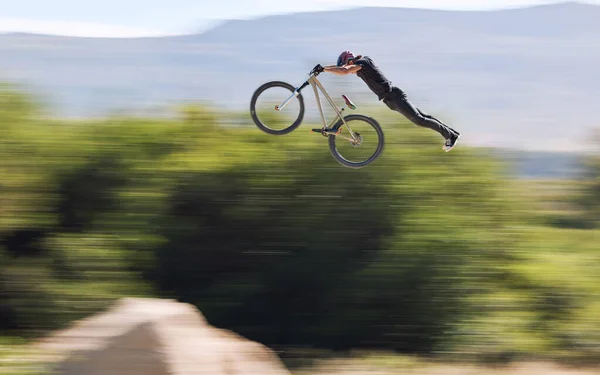 Young man showing his cycling skills while out cycling on a bicycle outside. Adrenaline junkie practicing a dirt jump outdoors. Male wearing a helmet doing extreme sports with a mountain bike.