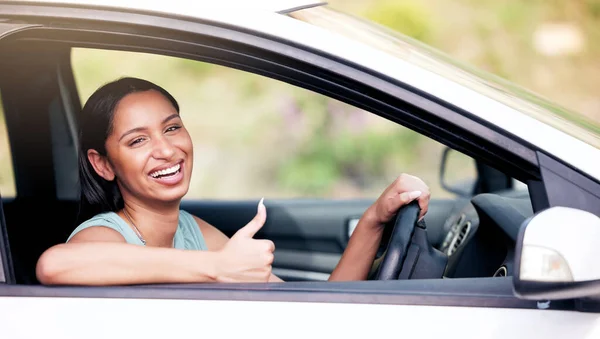 Cheerful mixed race woman showing thumbs up while driving her new car. Woman looking happy after buying her first car or after passing her drivers test. Car insurance.