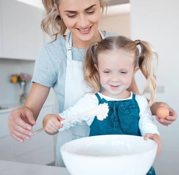 Mother and daughter baking at home. Happy mother and child bonding and cooking. Woman helping her daughter make batter. Young mother holding an egg, baking with her little girl