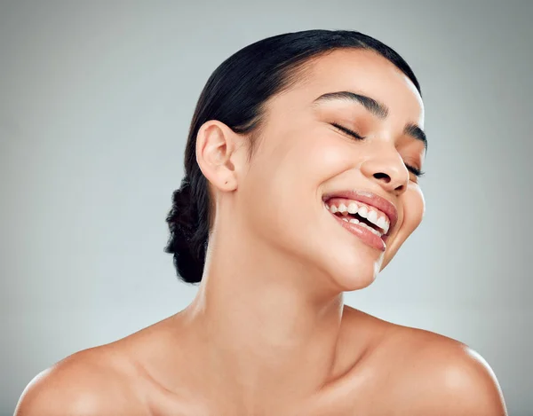 A beautiful young mixed race woman with glowing skin posing against grey copyspace background. Hispanic woman with natural looking eyelash extensions smiling while feeling her smooth skin in a studio.