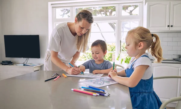 Young single caucasian mother helping her two cute little children with their homework in a bright kitchen. Two siblings doing their school project with their mom at home.