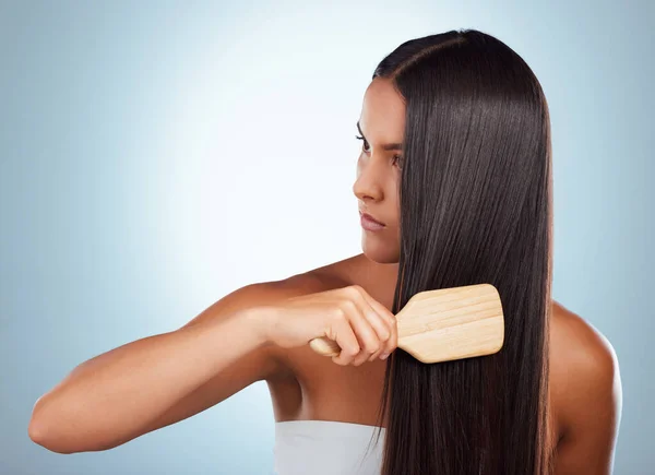 A beautiful young mixed race woman brushing her healthy strong hair against a grey studio background. Hispanic female grooming her hair.