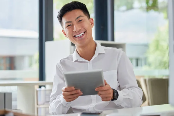 Young happy asian businessman using social media on a digital tablet sitting in an office at work. One chinese man smiling checking an email on a digital tablet. Man sending a message on a tablet.