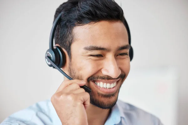 Closeup of smiling mixed race call centre agent smiling while wearing headset. Young male customer service representative using wireless headset and consulting clients online.