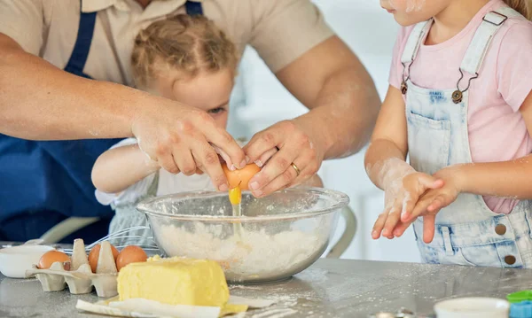 Father cracking egg into a bowl. Parent baking with his children. Family baking in the kitchen. Caucasian family baking together. Father bonding with his daughters and cooking. Kids baking together.