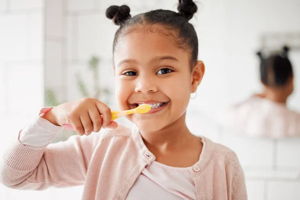 One mixed race adorable little girl brushing her teeth in a bathroom at home. A happy Hispanic child with healthy daily habits to prevent cavities and strengthen enamel.