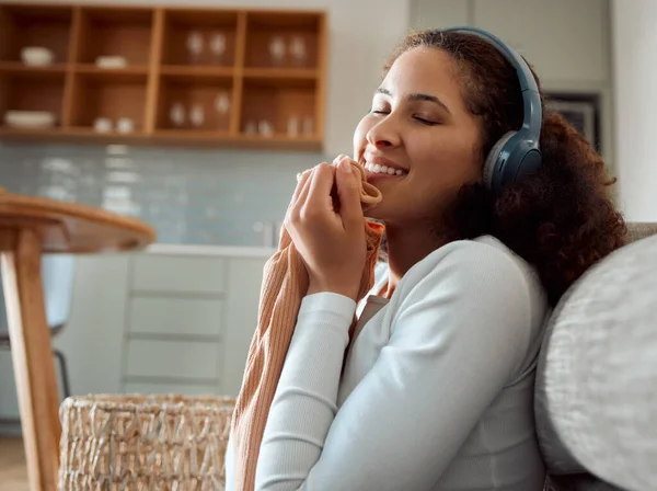 Woman enjoying the feel of a soft top. Young woman listening to music, cleaning laundry. Mixed race woman holding fresh, washed clothing. Happy woman rubbing clean clothing on her face.