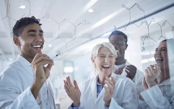 Diverse group of happy scientists clapping hands while writing and planning together on a board at work. Team of cheerful lab workers sharing ideas and brainstorming while standing together.