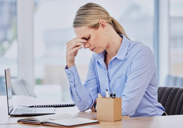Young frustrated caucasian business woman working at office desk suffering from chronic headaches while sitting in front of laptop. Female professional looking stressed and overworked.