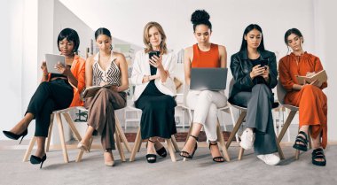 İş dünyasını kadınlar yönetiyor. Bir grup iş kadını iş yerindeki bir ofiste sırada oturuyorlar.