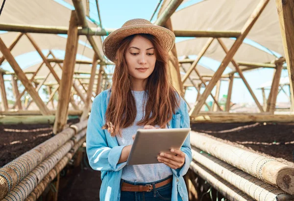 a young woman using a digital tablet while working on a farm.