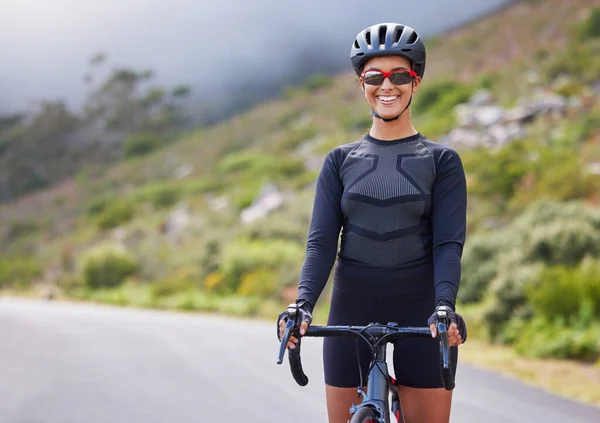 One athletic young woman cycling outside. Sporty fit female wearing a helmet and glasses while riding a bike along the mountain for exercise. Smiling and looking happy to be enjoying a hobby.