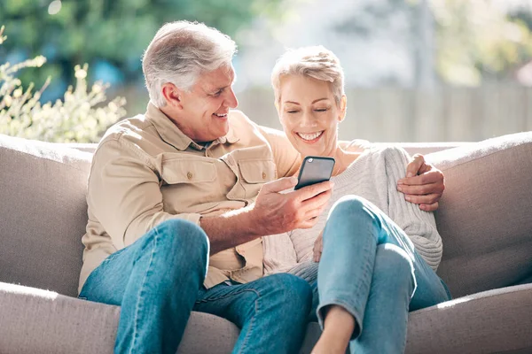 Care to share. a happy senior couple using a smartphone on the sofa at home