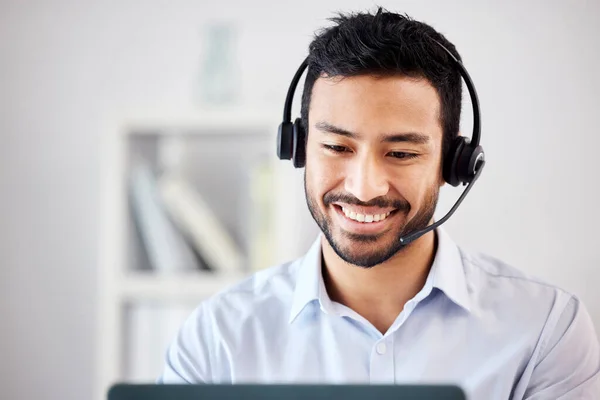 Young happy handsome mixed race male call center agent answering calls working on a laptop in an office alone at work. Hispanic Customer service agent on a call. Man using a laptop in sales.