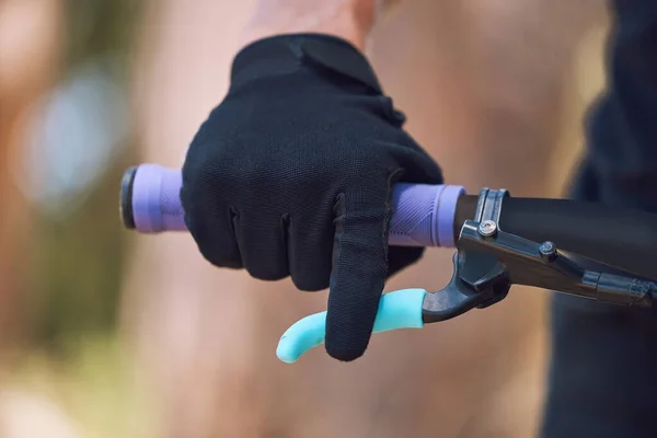 Closeup of an unknown cyclist with gloves holding the handle of his bicycle while cycling outside in nature. Athlete training and testing his brakes for safety before starting his cardio workout.