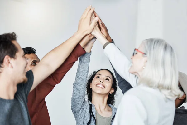 Diverse group of people standing together in circle and raising their hands in middle after therapy for a high five. Smiling support group celebrating successful session. Friends support mental health