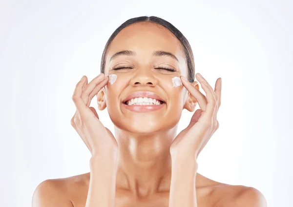 Happiness shines from the inside. a young woman applying moisturiser to her face against a studio background