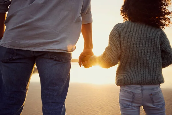 Closeup of father and little girl holding hands while watching the sunset together at the beach. Dad and young daughter showing affection, love and support by holding hands.