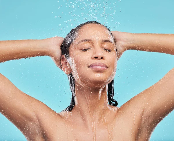 Let the water wash over you. a young woman washing her hair in the shower against a blue background