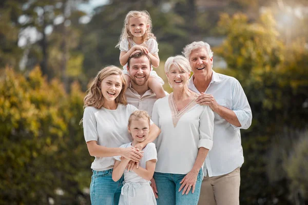 Portrait of a smiling multi generation caucasian family standing close together in the garden at home. Happy adorable girls bonding with their mother, father, grandfather and grandmother in a backyar.