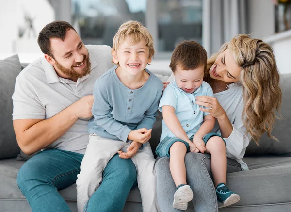 Carefree loving parents tickling and bonding with cute little laughing sons. Smiling caucasian family of four relaxing on the sofa at home.Playful young boys spending quality time with mom and dad.