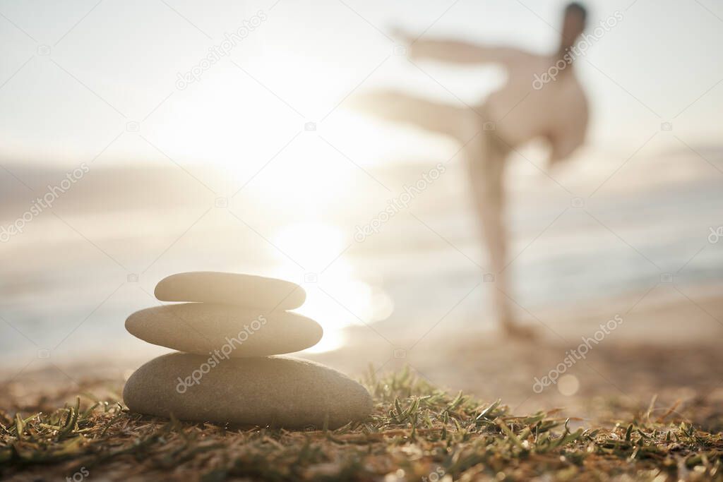 In balance there is harmony. Closeup shot of a stack of stones on the beach with a man practicing karate in the background