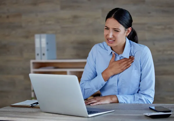 Young hispanic woman suffering from chest pain in office. Mixed race businesswoman feeling unwell while using a laptop at work.
