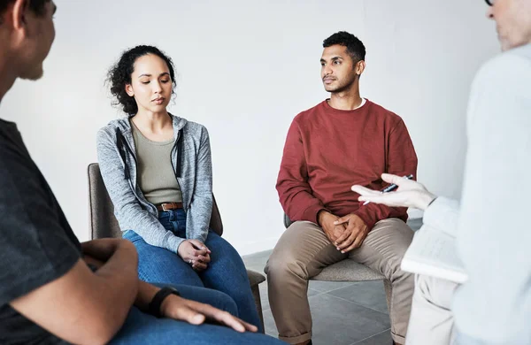 Close up of a young support group during meeting with professional therapist. Group of employees looking serious during a counselling session.