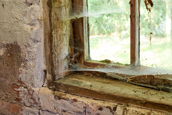 Interior view of an ancient house in need of TLC. An old window with dust and spiderwebs in an abandoned home inside. Architecture details of a windowsill frame with damaged rustic textures