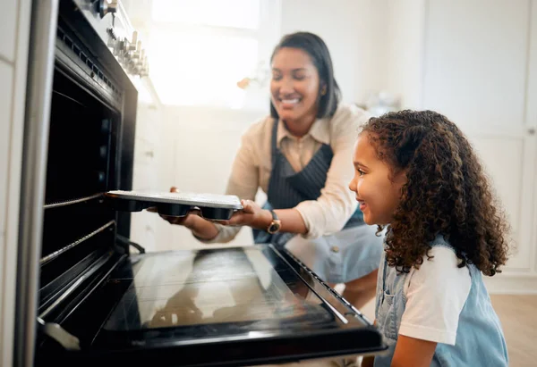 We create our own magic. a little girl watching her mother take a baking tray out of the oven