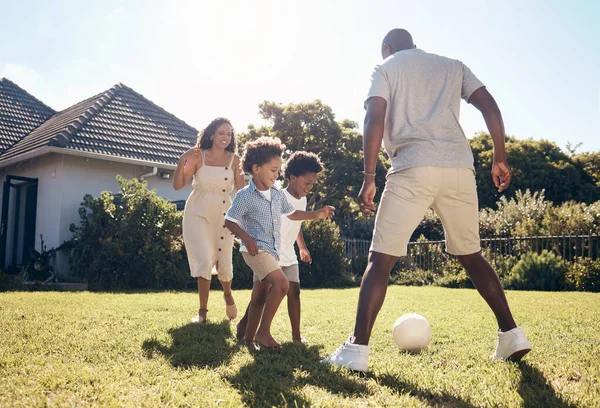 Happy mixed race family playing soccer outside in garden. Parents enjoying kicking a ball with their sons outside in the yard. Family bonding while playing together. Black family of four having fun.