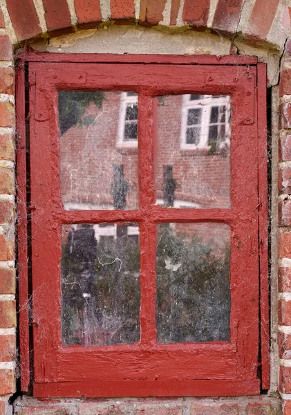 Closeup of an old dirty window in a red brick home. Zoom in on casement with red wood frame on a historic building with bumpy paint texture. Macro exterior details of windowsill in a traditional town.