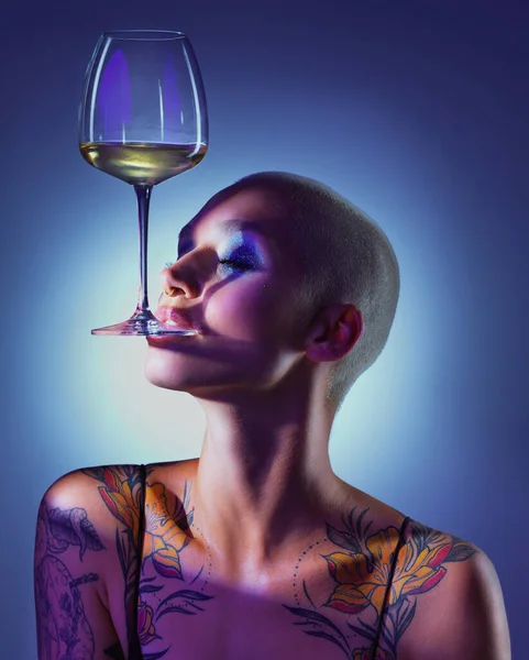 Im a goddess thats as fine as wine. Studio shot of an attractive young woman wearing edgy makeup and holding a glass of wine in her mouth against a blue background