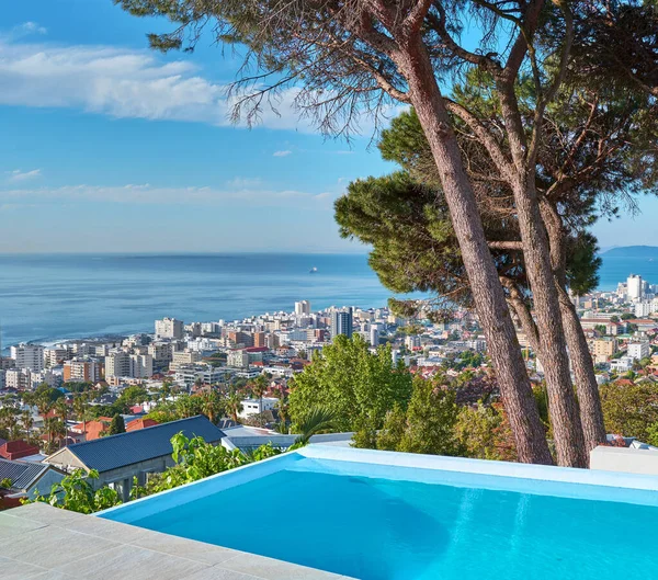 A blue pool on a luxury property with a coastal view of Cape Town and tourist landscape. The ocean and city against a clear sky horizon. A popular travel destination for tourists in South Africa.
