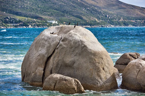 Big rocks in the blue ocean with mountains in the background. Stunning nature landscape or seascape on a summer day. Boulders or large natural stones in aqua sea water with beautiful rough textures.