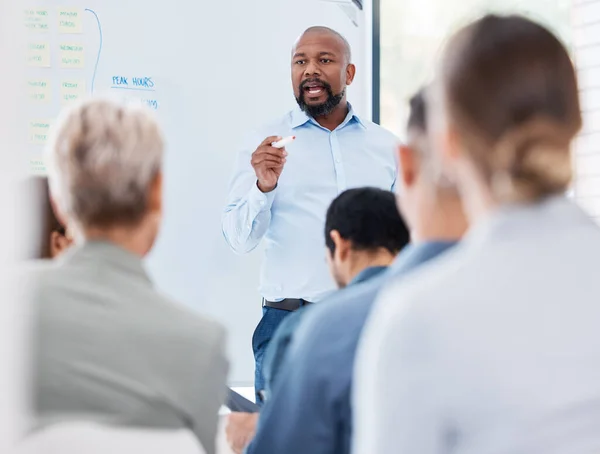 Mature african american business manager training and teaching team of colleagues in office. Black businessman using a whiteboard to talk and explain to diverse group of business people in workshop.