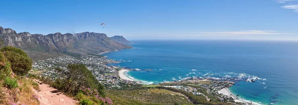 High landscape ocean view of mountains. Clear big blue sky and sea surrounded by nature and life creating peace and tranquility. An outdoor rocky path and waves against the coast around greenery