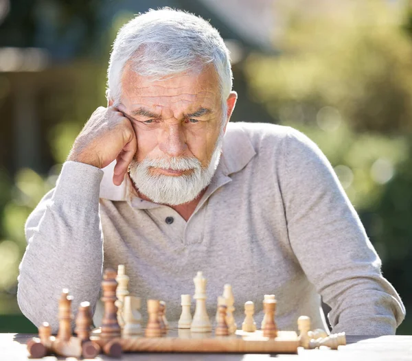 Where should I move next. a senior man sitting alone outside and looking contemplative while playing a game of chess
