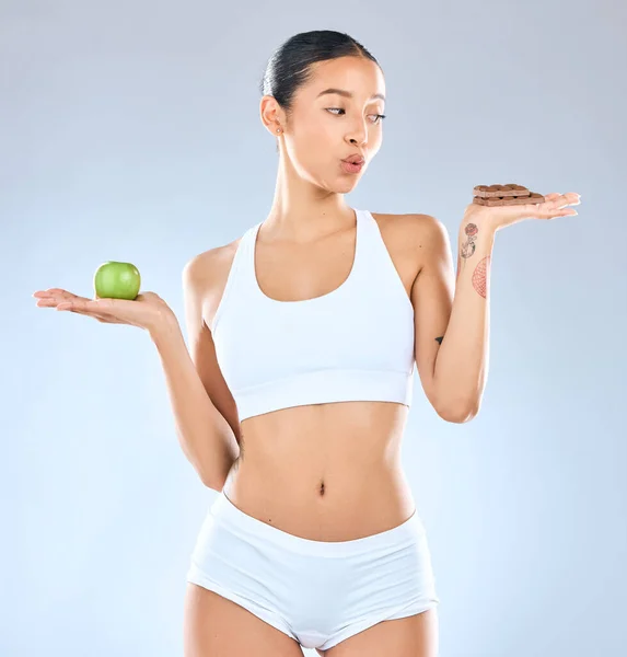 We DO have the ability to shapeshift. Studio shot of a young woman holding up a slab of chocolate and an apple in the other hand