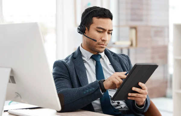 Lets tick that off our list. a young male call center agent using a computer and digital tablet in an office at work