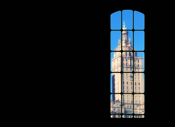 View from inside big window grid looking out at a traditional skyscraper building on blue sky copy space. Dark room with light part of a gothic vintage tower. Architecture of a tall built structure.