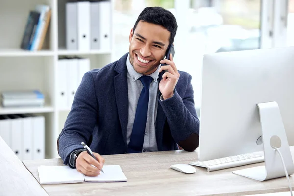 Ill call you back with feedback. a businessman talking on his cellphone and making notes while sitting at his desk