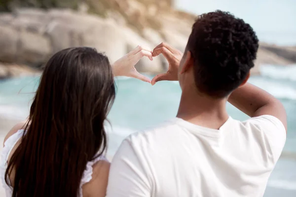 We share a love of the beach. an unrecognizable couple making a heart gesture with their hands at the beach