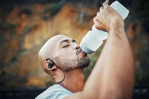 Exercise is the safest way to health. a sporty young man drinking water while exercising outdoors